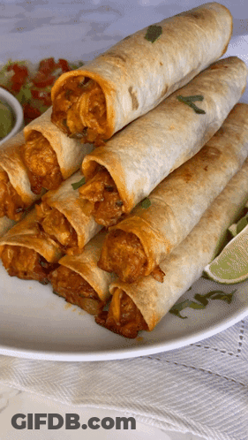 A White Plate Topped With A Stack Of Tacos And Lime Wedges GIF