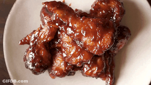 A White Plate Topped With Chicken Wings Covered In A Brown Sauce GIF