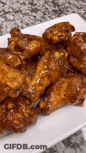 A White Plate Topped With Chicken Wings Covered In A Sauce GIF