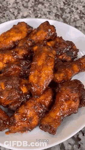 A White Plate Topped With Fried Chicken Wings With The Word Yum Written On The Bottom GIF