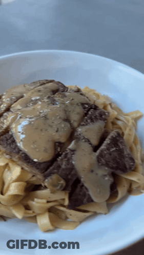 A White Plate Topped With Noodles And Meat With Gravy GIF