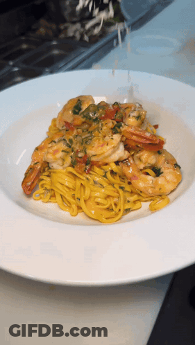 A White Plate Topped With Noodles And Shrimp On A Table GIF