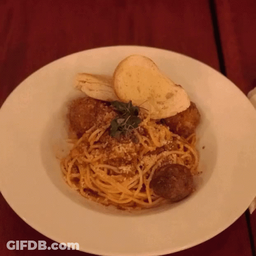 A White Plate Topped With Spaghetti Meatballs And Bread GIF