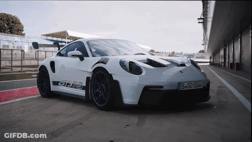 A White Porsche Gt3rs Is Parked On A Race Track GIF
