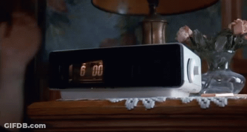 A White Radio Is Sitting On A Wooden Table Next To A Vase Of Flowers GIF
