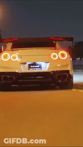 A White Sports Car Is Driving Down A Road At Night GIF