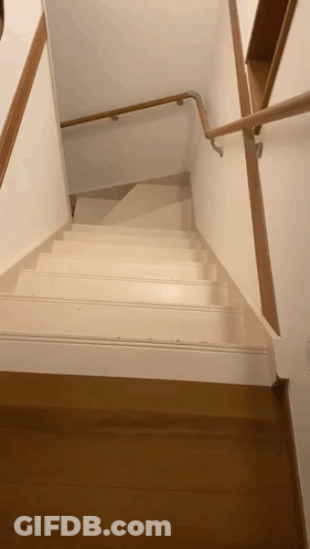 A White Staircase With A Wooden Railing And A Wooden Floor GIF