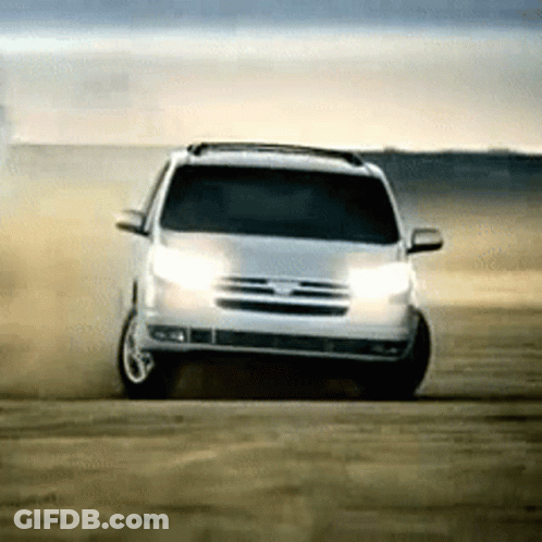A White Suv Is Driving On A Dirt Road With Its Lights On GIF