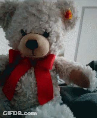 A White Teddy Bear With A Red Bow Around His Neck GIF