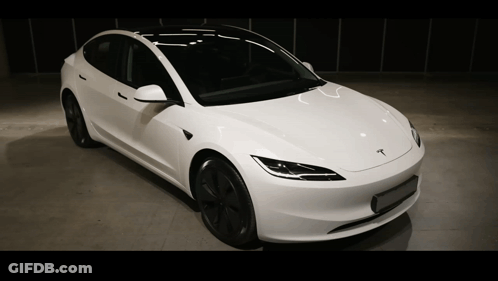 A White Tesla Is Parked In A Dark Room GIF