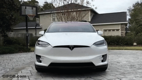 A White Tesla Is Parked In A Driveway In Front Of A House GIF