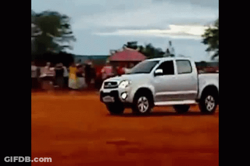 A White Truck Is Driving On A Dirt Road In A Field . GIF