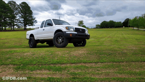 A White Truck Is Parked In A Grassy Field On A Cloudy Day GIF