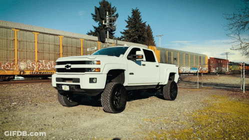 A White Truck Is Parked In Front Of A Train With Graffiti On The Side Of It GIF