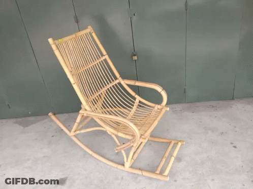 A Wicker Rocking Chair Sits On A Cement Floor In Front Of A Green Door GIF