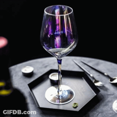 A Wine Glass With A Purple Stem Is Sitting On A Black Plate On A Table . GIF