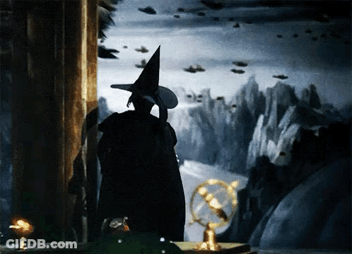 A Witch In A Witch Hat Stands In Front Of A Painting GIF