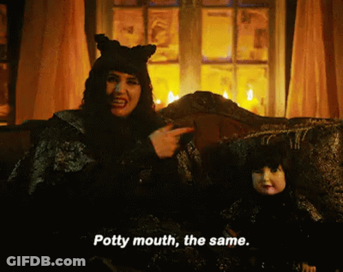 A Witch Is Sitting On A Couch Next To A Doll And Pointing At It . GIF