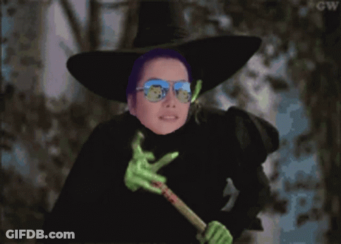 A Witch Wearing Sunglasses And A Purple Hat Is Holding A Green Wand GIF