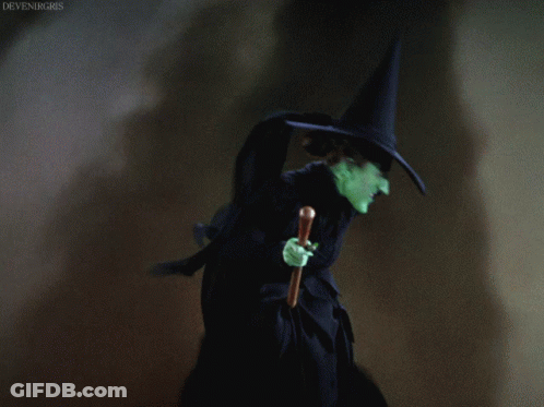 A Witch With Green Face And A Black Hat Holding A Cane GIF