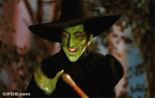 A Witch With Green Face Paint And A Black Hat Holds A Broom GIF