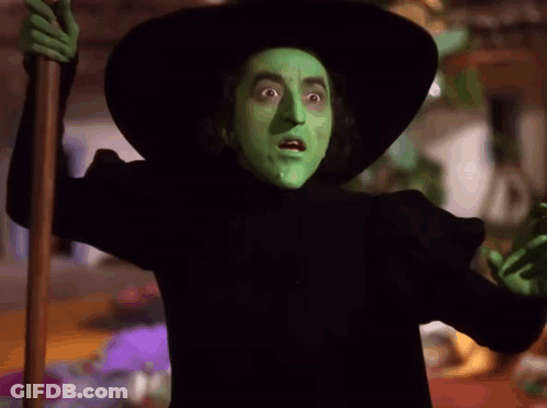 A Witch With Green Paint On Her Face Is Holding A Cane GIF
