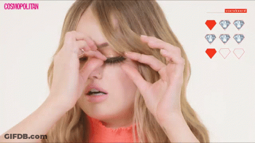 A Woman Adjusts Her Eyelashes In Front Of A Scoreboard With Diamonds GIF