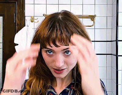 A Woman Adjusts Her Hair In A Bathroom With A Towel Hanging On The Wall GIF