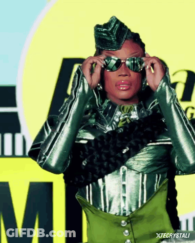 A Woman Adjusts Her Sunglasses In Front Of A Yellow Sign With The Letter M On It GIF