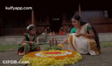 A Woman And A Little Girl Are Sitting On The Ground Making A Floral Arrangement . GIF