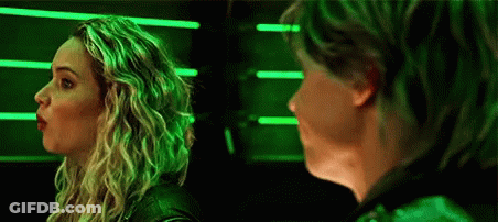 A Woman And A Man Are Standing Next To Each Other In Front Of A Green Light . GIF