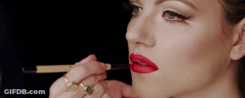 A Woman Applies Red Lipstick To Her Lips With A Brush GIF