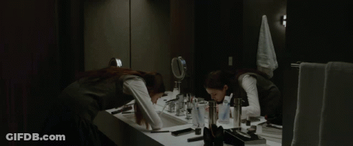A Woman Applying Makeup In Front Of A Mirror In A Bathroom GIF