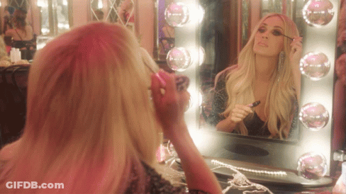 A Woman Applying Mascara In Front Of A Mirror With Pink Lights GIF
