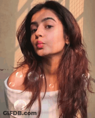 A Woman Blowing Bubbles In Front Of Her Face GIF