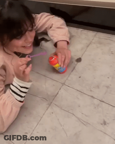 A Woman Blowing Soap Bubbles On The Floor With A Can Of Bubbles GIF