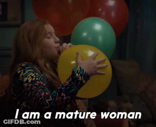 A Woman Blowing Up A Yellow Balloon With The Words " I Am A Mature Woman " Below Her GIF