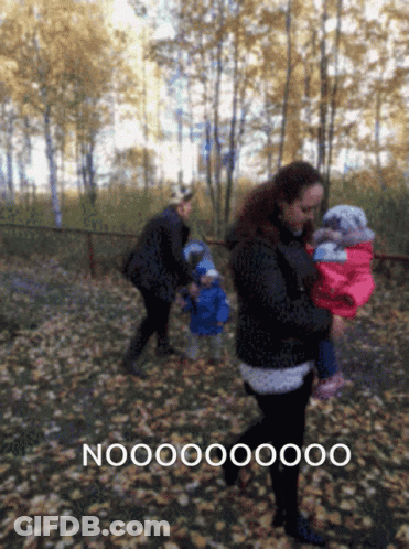 A Woman Carrying A Baby In A Park With The Word Nooo On The Bottom Left GIF