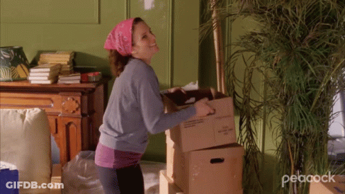 A Woman Carrying A Box With The Word Peacock On The Bottom Right GIF