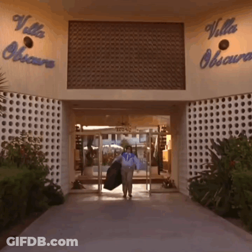 A Woman Carrying A Jacket Walks Into The Villa Obscura Building GIF