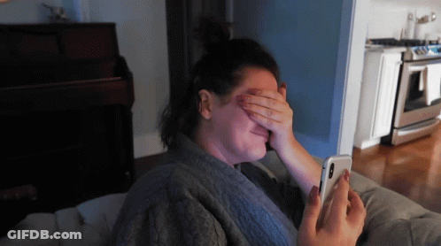 A Woman Covering Her Eyes With Her Hand While Looking At Her Cell Phone GIF