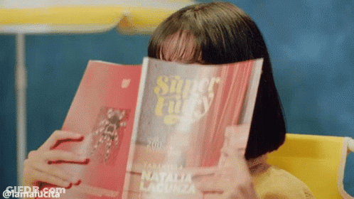 A Woman Covering Her Face With A Magazine Titled Super Lucky GIF