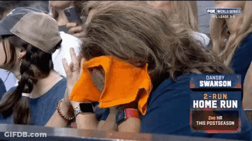 A Woman Covering Her Face With An Orange Towel While Watching A Baseball Game GIF