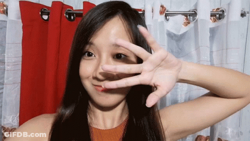 A Woman Covering Her Face With Her Hand In Front Of Red Curtains GIF