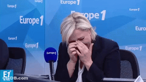 A Woman Covering Her Face With Her Hands In Front Of A Europe 1 Banner GIF