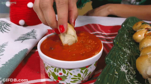 A Woman Dipping A Piece Of Bread Into A Bowl Of Sauce GIF