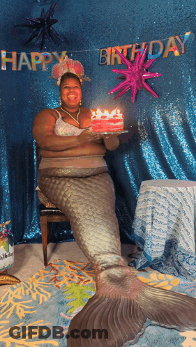 A Woman Dressed As A Mermaid Holds A Cake With Candles In Front Of A Happy Birthday Banner GIF