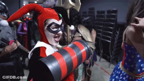 A Woman Dressed As Harley Quinn Is Holding A Red And Black Striped Object GIF