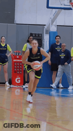 A Woman Dribbles A Basketball In Front Of A Gatorade Cooler GIF