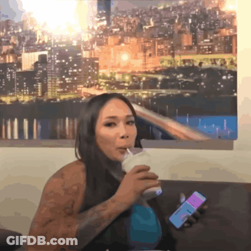 A Woman Drinking A Milkshake While Holding A Phone That Says ' I Love You ' On It GIF
